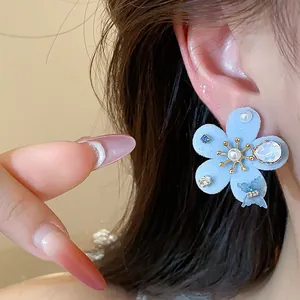 Primer plano de un elegante pendiente de flor azul flocado con perlas y circonitas