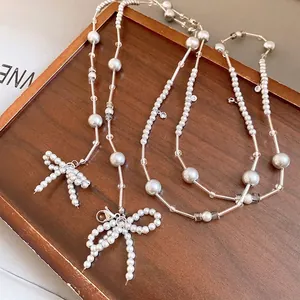 Elegante graue Perlenkette mit handgefertigten Schleifenanhängern auf einem Holztablett präsentiert