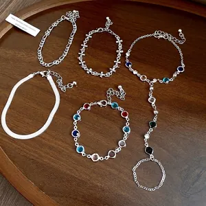 Set of five silver chain bracelets with multi-colored crystals on a wooden tray.