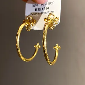 Detailed macro shot of gold C-shaped earrings featuring zircon fleur-de-lis designs