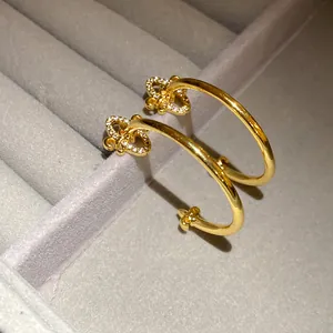 Macro detail of gold fleur-de-lis C-shaped hoop earrings with sparkling zircons