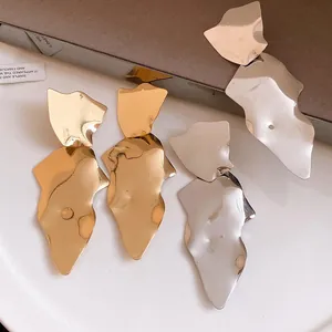 Detailed view of large irregular shiny metal drop earrings in gold and silver finishes