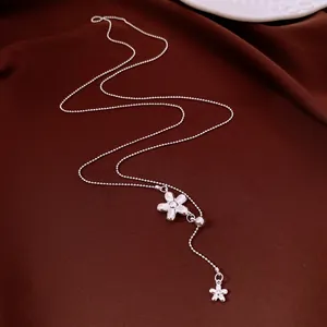 Detail shot of silver flower tassel necklace with delicate ball chain on brown fabric