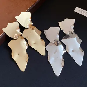 Close-up of large irregular metallic pendant earrings in gold and silver finish