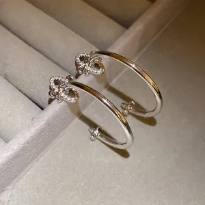 Close-up of silver fleur-de-lis C-shaped earrings with sparkling zircon in a jewelry box