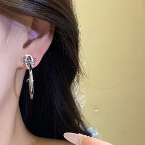 Detail of silver fleur-de-lis C-shaped earrings with zircon accents on ear