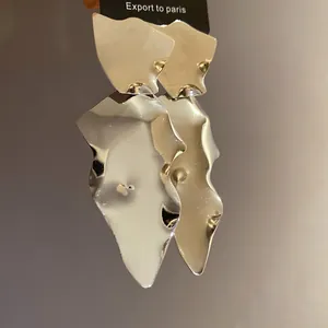 Close-up of large irregular silver metallic earrings with a reflective finish