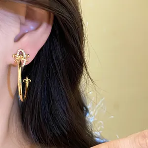 Detail view of gold C-shaped hoop earrings with zircon fleur-de-lis design on ear.