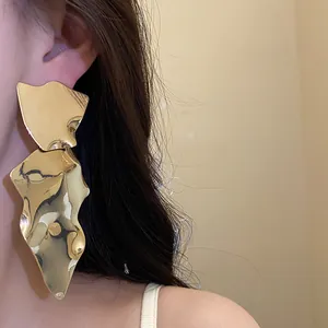 Detailed view of oversized irregular gold metallic earrings worn on an Asian model.