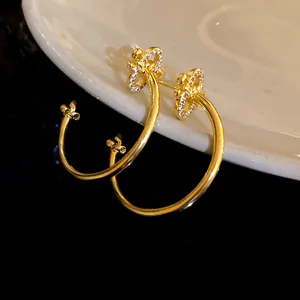 Close-up detail of gold-plated fleur-de-lis hoop earrings with sparkling zircon