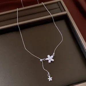 Detailed view of a silver flower tassel necklace presented on a brown jewelry display tray.