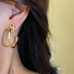 Detailed close-up of elegant gold fleur-de-lis C-shaped hoop earrings with zircons on model ear