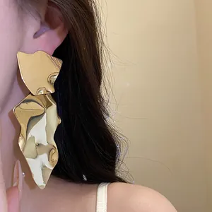 Close-up detail of a large irregular metallic gold drop earring with high shine