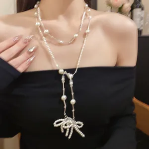 Nahaufnahme einer eleganten weißen Perlenhalskette mit Schleifenanhänger an einem Modell