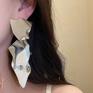 Detailed view of large irregular metallic silver drop earrings worn by a model in soft light