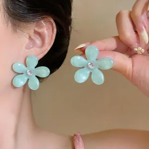 Primer plano de un pendiente de flor de resina verde claro con circón en la oreja de modelo.