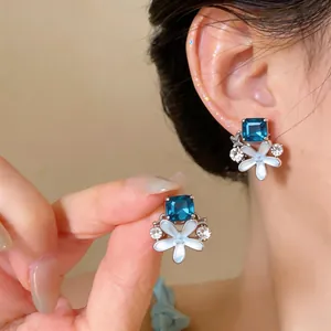 Close-up detail of elegant blue crystal flower stud earrings with white enamel petals