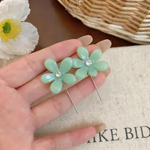 Primer plano de pendientes de flor de resina verde claro con detalle de circón
