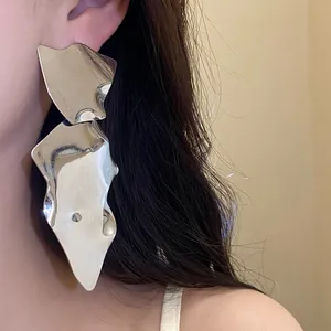 Detailed view of oversized irregular glossy silver metallic drop earrings on model ear