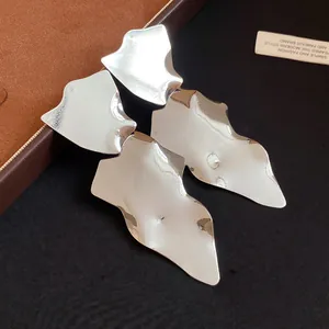 Close-up of irregular silver metallic glossy pendant earrings on a luxury display box.
