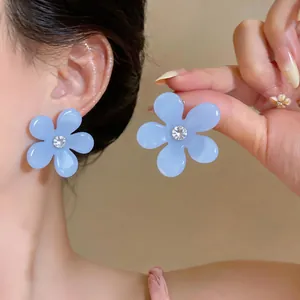 Primer plano de pendientes de flor de resina azul con circón en la oreja y mano