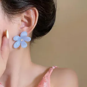 Primer plano de un pendiente de flor de resina azul claro con un centro de circonita