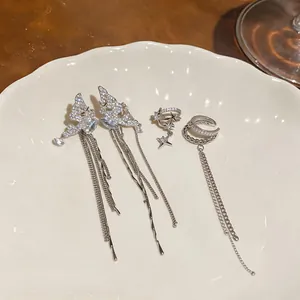Detail shot of silver-toned zircon ear cuffs and long tassel butterfly earrings on white plate.