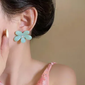 Primer plano de un pendiente de flor de resina verde menta con circonita en el modelo.