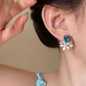Detail view of a dainty silver needle earring with blue stone and flower design.