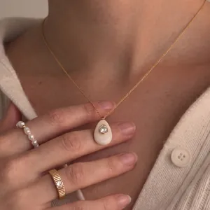 Gros plan d'un collier pendentif goutte en résine avec cristal et bague en or texturée chic