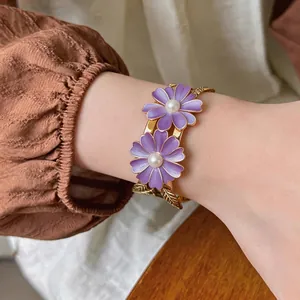 Elegant golden bangle featuring purple enamel daisies with pearl centers and leaf details