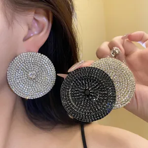Primer plano de pendientes circulares grandes con pedrería en plata, oro y negro elegante.
