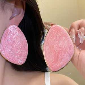 Dettaglio di grandi orecchini geometrici irregolari rosa marmorizzato con bordo dorato