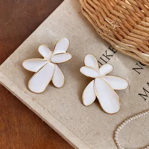 Elegant large white floral stud earrings with gold trim on vintage fabric background