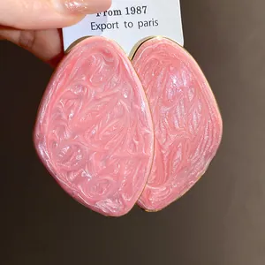 Dettaglio macro di orecchini geometrici irregolari smaltati rosa con trama marmorea.