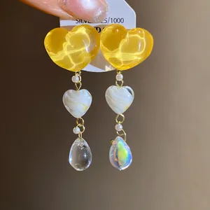 Primo piano dettagliato di orecchini a cuore in resina gialla e goccia iridescente