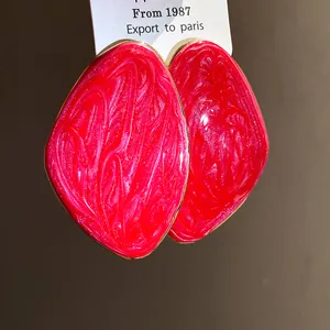 Primo piano di orecchini smaltati rosa vivace con una forma geometrica irregolare.