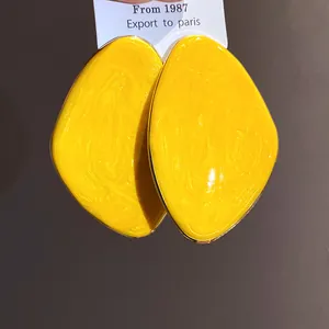 Primo piano di orecchini geometrici irregolari in smalto giallo brillante dal gusto vintage.