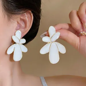Detailed close-up view of elegant large white enamel flower earrings with gold borders