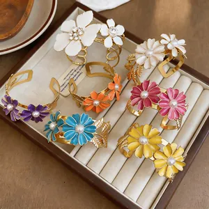 Detailed view of colorful enamel daisy cuff bracelets with pearl centers in a tray