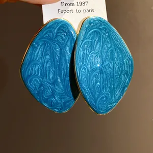 Primo piano di orecchini geometrici in smalto blu con bordi dorati retrò.