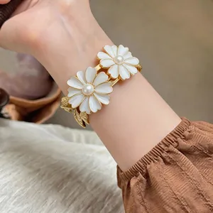 Detailed view of white daisy bangle with pearl center on wrist, elegant gold finish