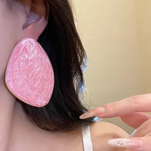 Dettaglio di un orecchino geometrico in smalto rosa marmorizzato con eleganti unghie lunghe.