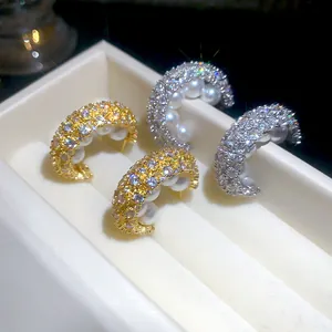 Nahaufnahme von C-förmigen Ohrstecker mit Mikro-Zirkonia und Perlen in Gold und Silber.