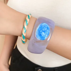 Close-up of chunky lavender resin bangle and teal enamel swirl bracelet on wrist