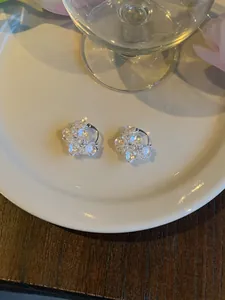 Detailed macro view of elegant silver floral hoop earrings with zircons on a white plate.