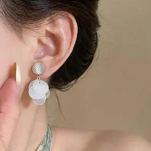 Detail shot of elegant drop earrings featuring white shell-style discs and gold textured studs