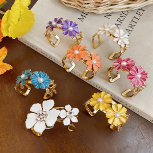 Detailed view of colorful enamel daisy cuff bracelets with pearl centers on a rustic background.