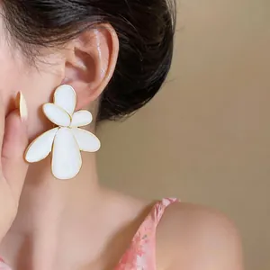 Close-up detail of oversized white enamel flower stud earring with gold-tone border.