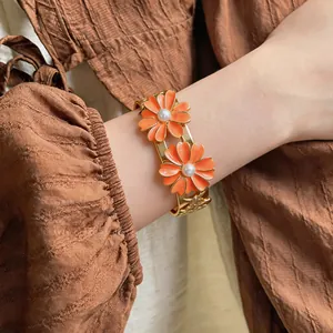 Detailed view of a gold-tone bangle featuring orange enamel daisies and central pearls.
